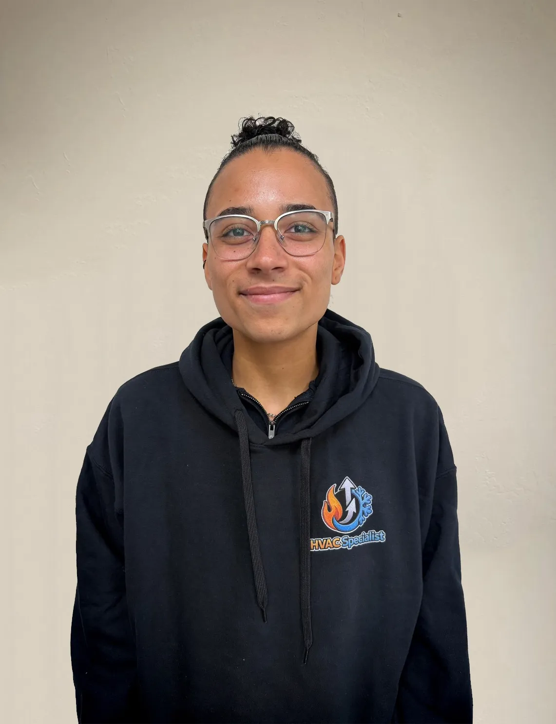 Danni Bezanson smiling in a black hoodie with the text "HVAC Specialist" and company logo on the front, standing against a light neutral wall. Portrait of the Marketing Operations Manager.