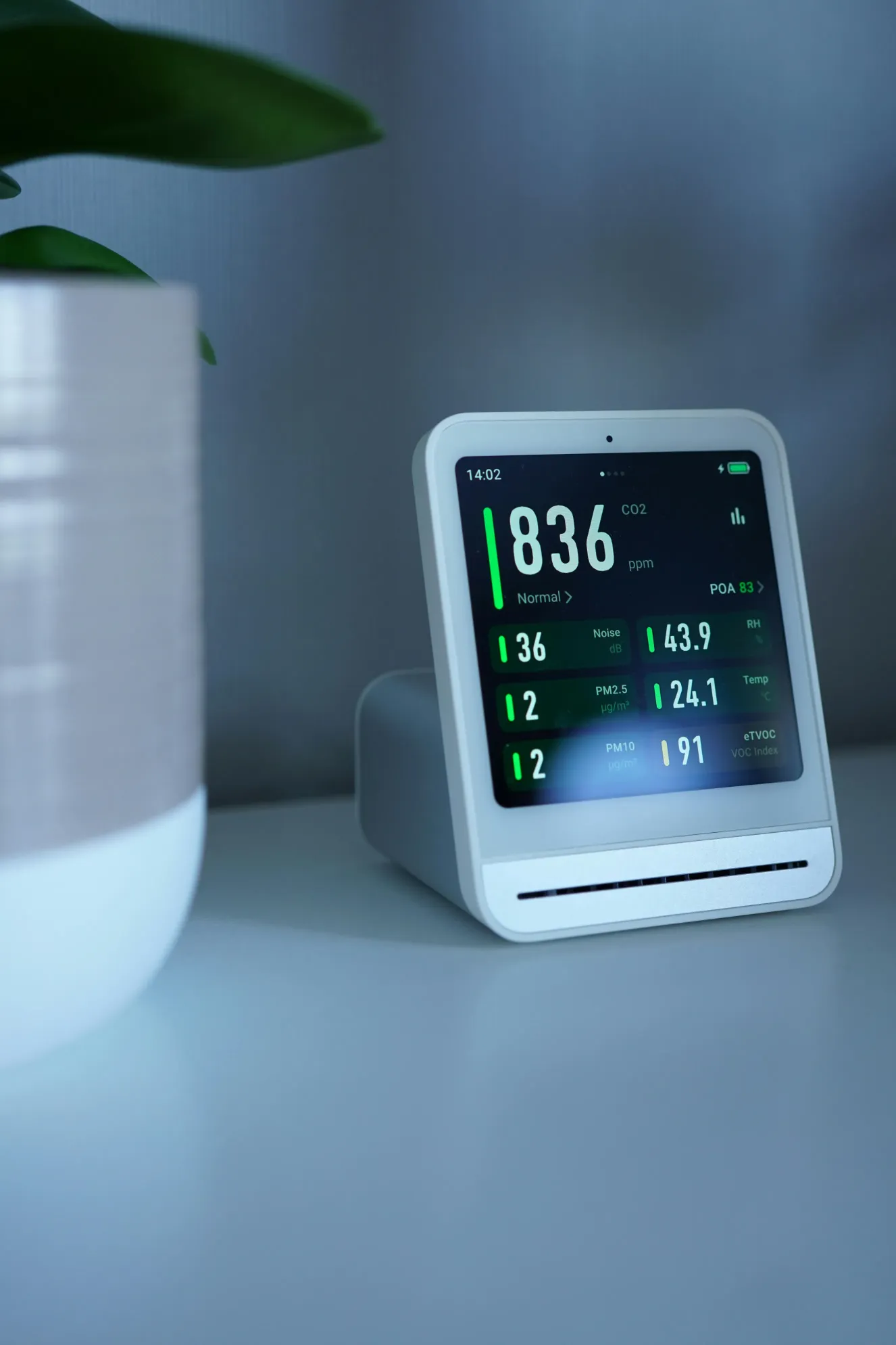 Digital air quality monitor on a tabletop displaying CO2, humidity, temperature, and particle readings. The device represents Indoor Air Quality Solutions for tracking healthier indoor conditions.