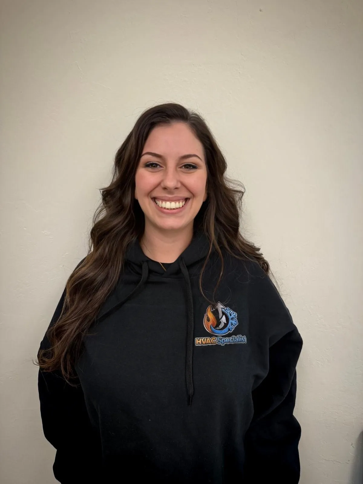 Rochelle Nilsson wearing glasses and a black hoodie with the text "HVAC Specialist" and company logo on the front, standing against a light neutral wall. Portrait of the Chief of Operations.